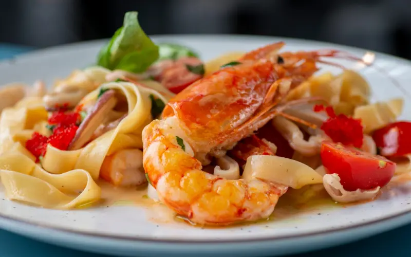 Des tagliatelles aux crevettes, calamars et poivrons servies dans une assiette blanche.