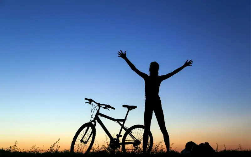 La silhouette d'une personne, bras levés à côté de son vélo, devant un ciel de lever du jour.