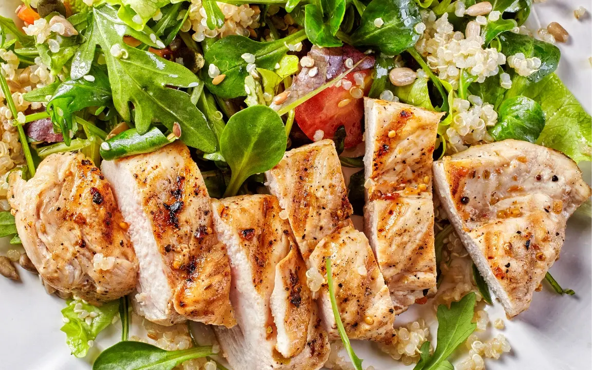 Des aiguillettes de poulet grillé disposées sur une salade de quinoa, jeunes pousses et tomates.