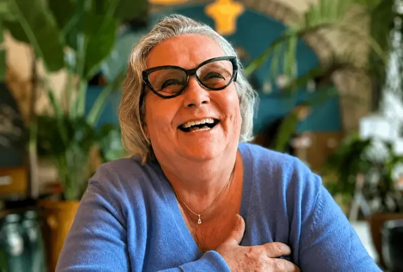Chantal, souriante, une main posée sur la poitrine, chez elle devant ses plantes.