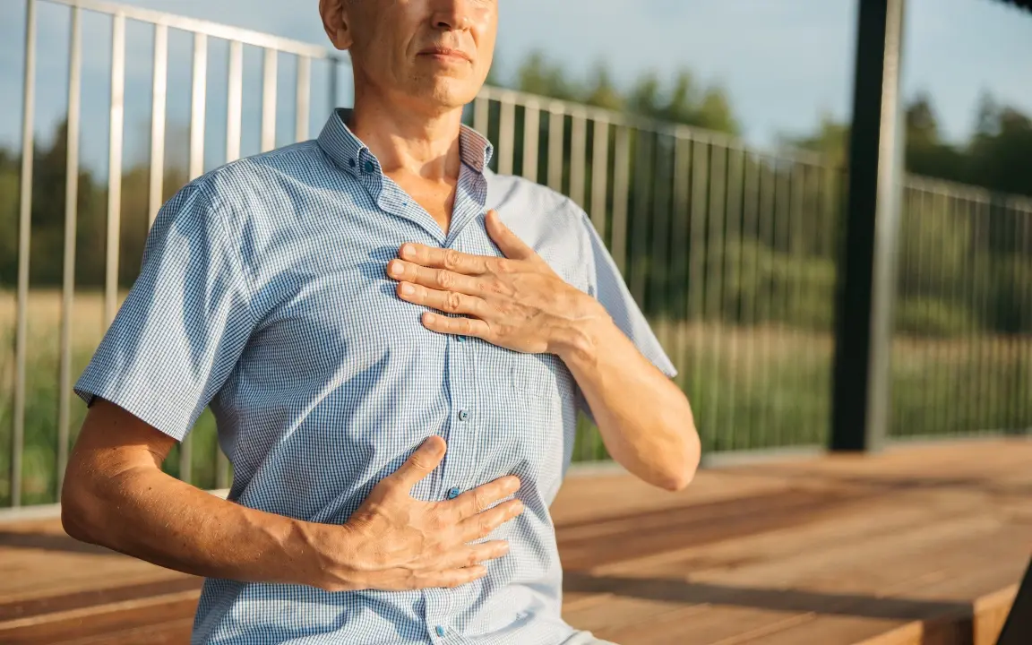 Un homme, une main sur la poitrine et l'autre sur le ventre, respire lentement sur une terrasse.