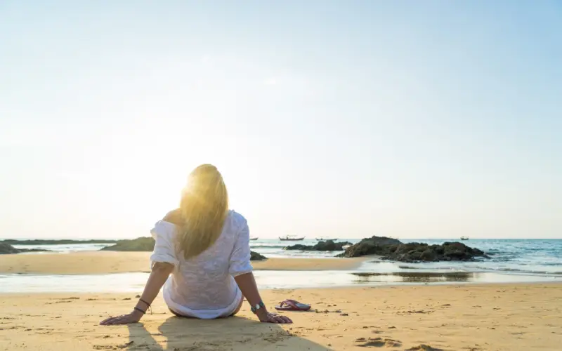 A woman sits alone on the sand, looking out at the sea.