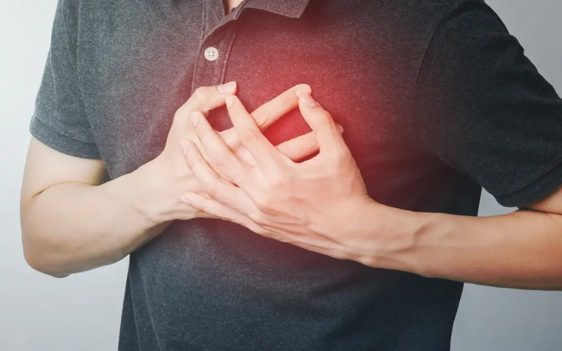 A man presses both hands to his chest, a red glow marking the pain over his heart.