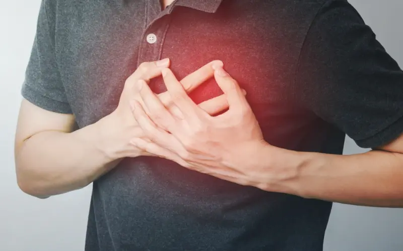 A man presses both hands to his chest, a red glow marking the pain over his heart.